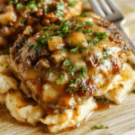 Golden-brown seared pork chops nestled in a creamy mushroom and onion gravy, garnished with fresh parsley, served on a rustic ceramic plate with soft steam rising—background is light wood countertop with subtle natural lighting.
